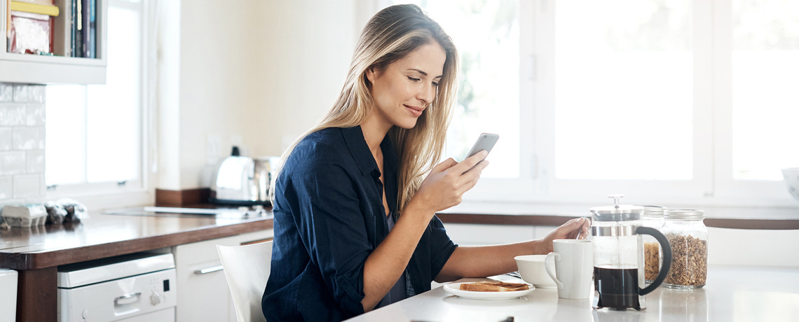 Frau mit Smartphone am Frühstückstisch liest die neuesten Nachrichten mit der News App der NNN